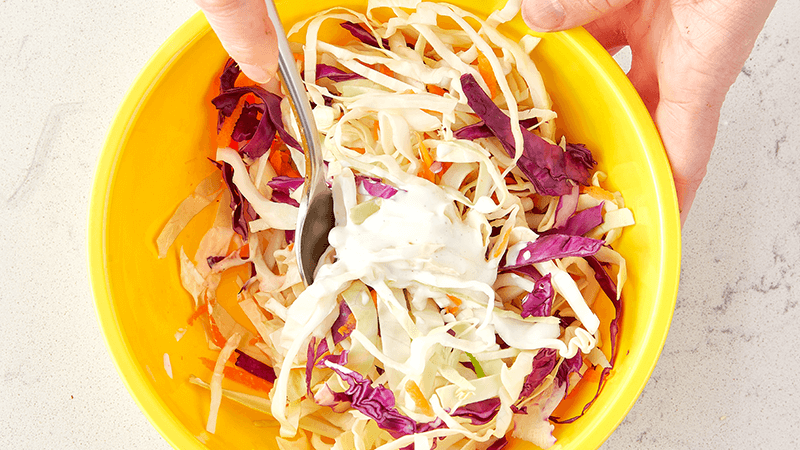 shredded cabbage, carrot & mayo mixing in a yellow bowl