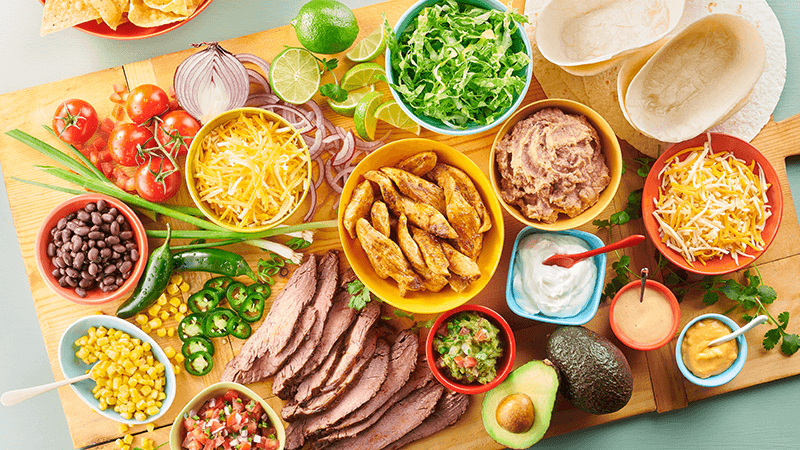 various taco fillings such as beef, chicken, beans, cheese, avocado etc. placed on wooden board