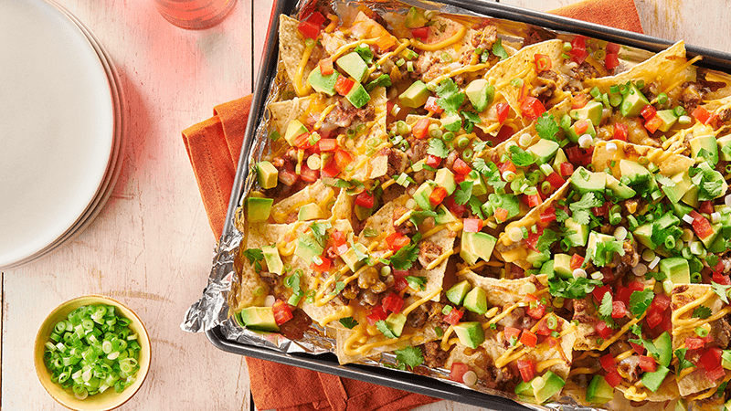 easy beef nachos garnished wit avocado & spring onion served in a pan