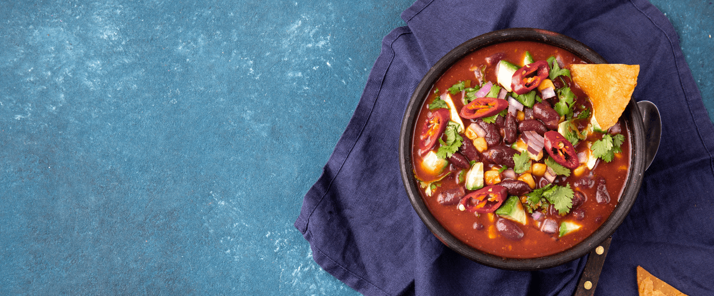 a bowl of mexican chili bean soup garnished with veggies, coriander and a tortilla chip on blue napkin with rustic background