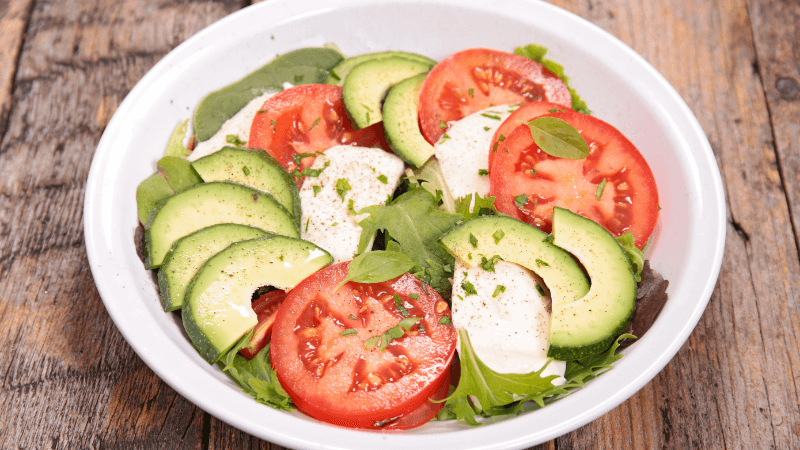 Tomato, avocado, and mozzarella salad sprinkled with salt and pepper served in a white plate