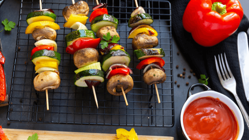 grilled vegetable skewers placed on grill near to red pepper and fork