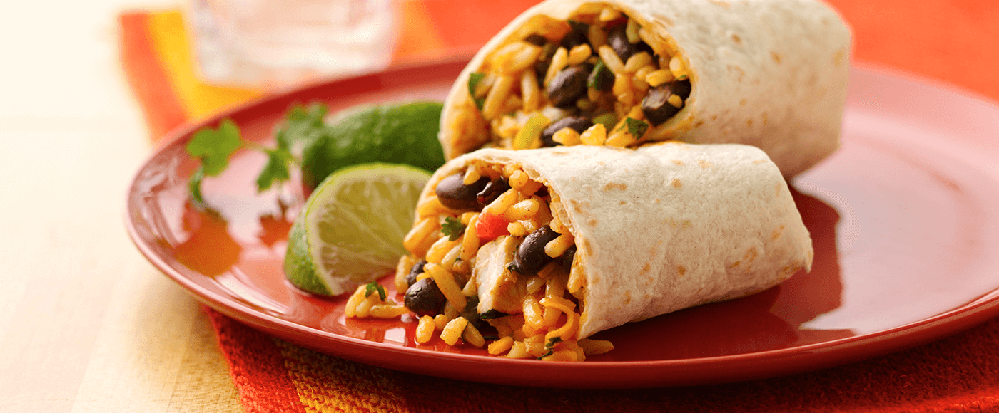 Chicken and black bean burritos served on red plate garnished with lemon & coriander