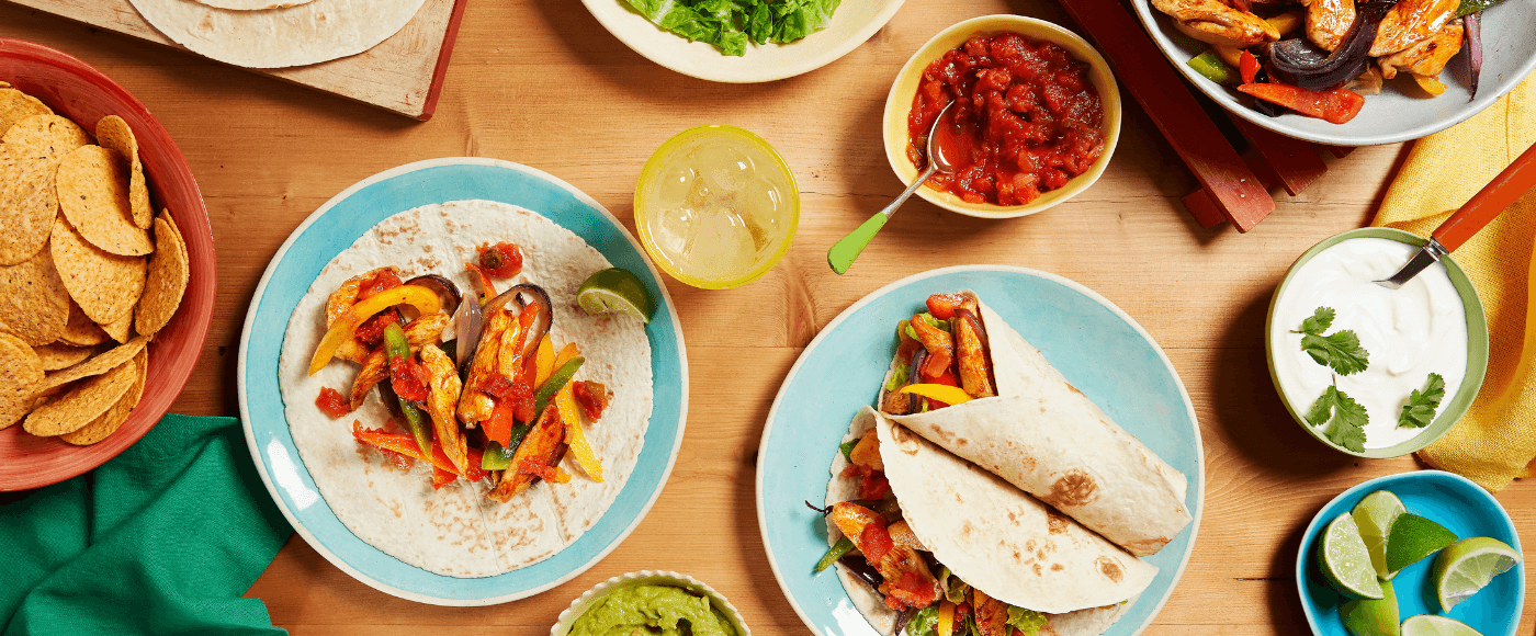a colourful Mexican meal with chicken fajitas, tortilla chips, salsa, guacamole, sour cream & lime wedges