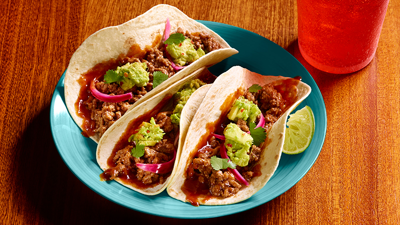 Three tacos placed in a blue color dish on a wooden table.